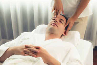 Beyaz adam stres önleyici kafa masajından ve lüks bir tatil beldesi veya otel spa salonundaki modern ışık ortamında yüz güzelliği eğlencelerini şımartmaktan hoşlanıyor. Sessiz.