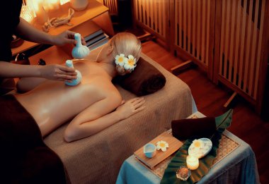 Sıcak bitkisel top spa masaj vücut tedavisi, masör kadın vücuduna nazikçe şifalı bitki torbası bastırıyor. Aromaterapi tesisinin sakinliği ve dinginliği kaplıca salonundaki mumların sıcacık ışığında. Sessiz.