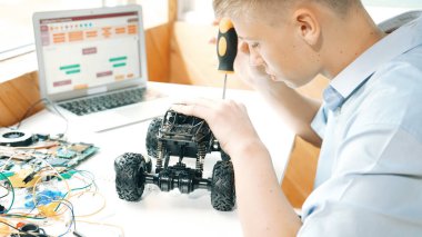 Elektronik ekipman ve dizüstü bilgisayar görüntüleme programı olan mutlu öğrenci çalışma arabası modeli inşaatının üst görüntüsü STEM sınıfında dağılıyor. Yaratıcı eğitim. Öğretim.