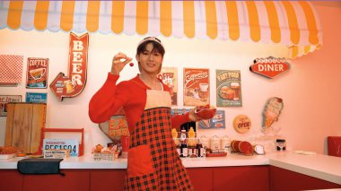 Profesyonel Asyalı restoran işçisi yemek hazırlar ve yemek barının arkasında durur. Kırmızı önlüklü çekici garson kameraya bakarken vişne topluyor. Çılgın dans. Mutluluk.