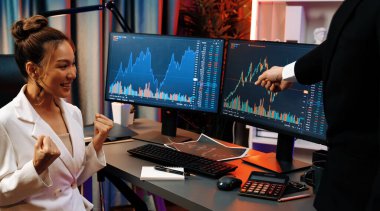 Başarılı tüccarlar, bilgisayar ekranındaki dinamik finansal grafiğe işaret ederek, neon ışıklı modern ofiste gerçek zamanlı olarak en yüksek kârlı görünen borsa ile yumruklarını kaldırıyorlar. İnfobahn.