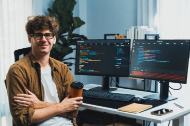 Kameraya bakan ve elinde kahve fincanı tutan çevrimiçi yazılım geliştirme teknolojisi geliştiricisi bilgisayar ekranlarını çevreleyerek, modern merkez ofisteki son sürüm için yeni programlama üzerinde çalışıyor. Toplayıcı.