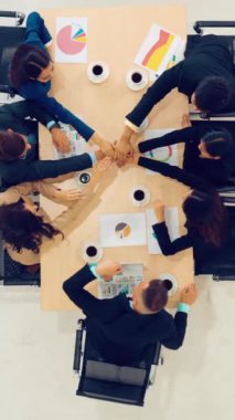 Mutlu iş adamları takım çalışmasının başarısını kutlarken ofis masasında yukarıdan çekilen neşeyle kutluyorlar. Genç işadamı ve işkadını işçiler birlik ve destek göstererek neşeli bir zafer kazandılar. .