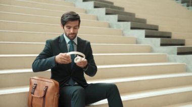 Profesyonel iş adamlarının yakınları kulaklık kullanarak müzik dinlemeyi severler. Akıllı proje yöneticisinin portresi merdivenlerde otururken kulaklık takıyor. İyi haberler almak, terfi almak. Sevinçli..