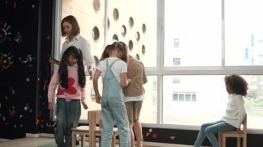 Çeşitli çocuklar sandalye kapmaca oynarken genç ve güzel öğretmenler müziği kapatıyor. Çok kültürlü öğrenciler yaratıcı aktivitelerde sandalyede koşup oturuyorlar. Müzik dersi. Etkinlik.