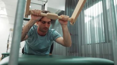 Eğitmen rehberliğinde Pilates Cadillac üzerine bar tabanlı alıştırma yapan bir müşteri. Erkek öğrenci, üst vücut gücünü arttırmak için Cadillac 'ın üzerinde kuğu esnetiyor. Alışkanlık.