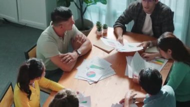 Zeki insanların kağıt fırlatıp finansal dökümanlar ve etrafa dağılmış borsa analiz kağıtlarıyla toplantı masasında beşlik çakması. Ekibin hava görüntüsü projeyi kutluyor. Sempozyum.