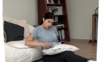 Kanepede oturan bir kadın ders kitabı okuyarak sosyal ve mesleki teknoloji bilgisini artırır ya da akıllı bir anne olmak için çocuk yetiştirir. Hayat boyu öğrenme konsepti. Uyumsuzluk.