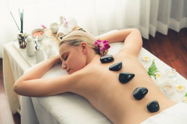 Lüks tatil köyündeki kaplıcalarda sıcak taş masajı. Gün ışığı sükunet ortamında, mutlu kadın müşteri bazalt taş masajından zevk alıyor. Rahatlatıcı bir sıcaklıkla vücudun üzerinde süzülüyor. Sessiz.