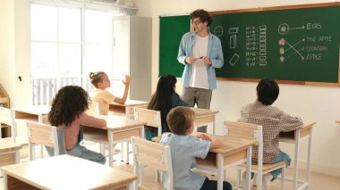 Çeşitli ilkokul öğrencileri öğretmenleri çocuğa bakarken sınıfta yürüyorlar. Profesyonel eğitmen tahtaya çıkıp öğretmenlik yapmaya hazırlanırken sevimli çocuklar sınıfa katılıyor. Pedagoji.