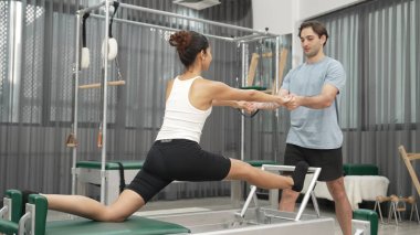 Esneklik ve çekirdek eğitimi için pilates kursunda trapez masasında destek alan bir kadın. Öğrenci dengeyi geliştirmek için reformcuları iki büklüm ediyor. Alışkanlık.