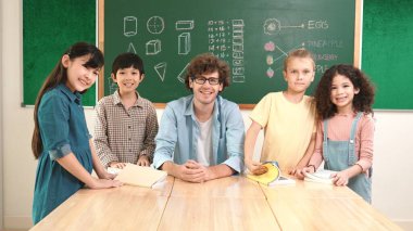 Profesyonel Kafkas öğretmeni ve çeşitli öğrenciler kameraya bakarken mutlu okul çocuğu gülümsüyor. Sınıfın önünde dururken gülümseyen bir grup çok kültürlü çocuk. Eğitim. Pedagoji.