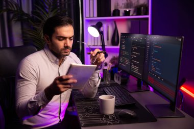 Akıllı bilişim geliştiricisi bilgisayar ekranında yazılım geliştirme kodlaması üzerinde çalışıyor ve en yeni uygulama projesinin notlarını okuyor, program güncellemesi düşünüyor neon ışıklı siber ofiste online web sitesi verileri. Tahmin et..