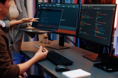 Modern ofisteki neon ışık odasında bilgi ağını gösteren dizüstü bilgisayarla iki ekranda veri çalıştıran akıllı web sitesi geliştirme kodlayıcı sistemini tartışan IT geliştiricilerinin ciddiyeti. İnfobahn.