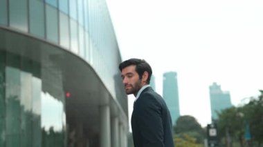 Profesyonel iş adamı hareket ediyor ve kameraya bakarken ayakta duruyor. Gülümseyen yönetici kameraya kendinden emin bir şekilde gülümsüyor. Mimari binada takım elbiseli yatırımcıların yakın çekimi. Sevinçli..