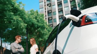 Genç çift yazın yeşil sürdürülebilir şehir bahçesinde elektrikli araba ile geziyor. Elektrikli aracın iç organlarının temiz yeniden şarj edilebilir enerjisi için kentsel sürdürülebilirlik yaşam tarzı olarak.