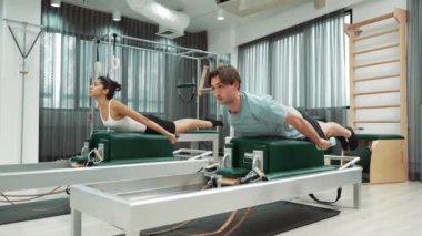 Erkek ve kadın spor salonunda vücut ve sırt kaslarını güçlendirmek için pilates sandalyesi üzerinde egzersiz yapıyorlar. Pilates partneri sırtının üst kısmını güçlendirmek için yenilikçi olmaya eğilimli. Alışkanlık.