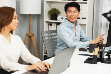 Gülümseyen Asyalı bir adam, yan görüntüdeki modern ofis çalışma masasında veri tabanını ararken günlük dizüstü bilgisayarla pazarlama raporu projesini planlarken kadın meslektaşıyla konuşuyor. İnfobahn.