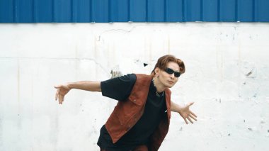 Beyaz arka planda break dans pratiği yapan yakışıklı bir sokak dansçısı. Hip hop tarzı giyinen sporcu, mavi arka planlı bir sokakta müzik eşliğinde ayak sesleri çıkarıyor. Açık hava sporu 2024 hiphop..