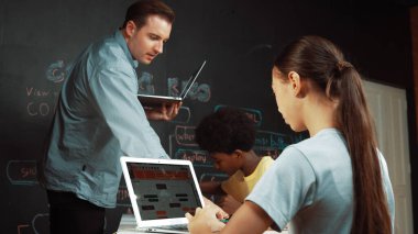 Afrikalı erkek manken tamir ederken beyaz kız programlama ya da kodlama sistemi. Öğretmen elinde dizüstü bilgisayar tutarken çeşitli çocukların web geliştirme programı yazmalarına bakıyor. Yenilik eğitimi. Öğretim.