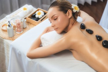 Lüks tatil köyündeki kaplıcalarda sıcak taş masajı. Gün ışığı sükunet ortamında, mutlu kadın müşteri bazalt taş masajından zevk alıyor. Rahatlatıcı bir sıcaklıkla vücudun üzerinde süzülüyor. Sessiz.