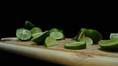 Yakın plan, canlı bir dilim taze kireç kırsal bir ahşap kesme tahtasının üzerinde duruyor. Tazelik ve canlılık yayıyor. Kesme tahtasına konmuş yeşil limon diliminin yarı saydam zarları. Geliştirilebilir.