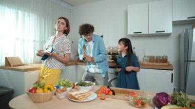 Beyaz yetenekli baba, anne ve Asyalı kız birlikte dans ederken kahvaltı hazırlıyorlar. Modern mutfakta sebze hazırlarken ukulele çalan yetenekli bir anne. Sağlıklı gıda konsepti. Pedagoji.