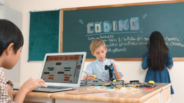 Kafkas arkadaşı STEM sınıfında elektrik panosunu tamir ederken Asyalı çocuk kodlama programı. Enerjik öğrenci kodlama mühendisliği komut yazarken ve yapay zeka yazılımını programlarken tahtada duruyor. Pedagoji.
