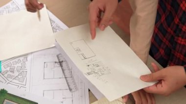 Mimari döküman, ölçüm araçları ve ahşap blokların modern ofiste etrafa saçıldığı masa üzerine planlar yapma konusunda akıllı mimar ve güvenlik mühendisi tartışması. - Yakın çekim. Tanımlama.