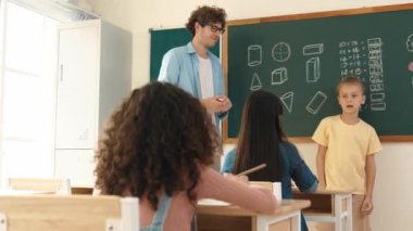 Profesyonel öğretmen konuşuyor ve sınıfta Asyalı çocuğa fikrini açıklıyor. Sınıfın önünde karatahta matematik dersiyle dikilmiş beyaz öğrenci dinleme eğitmeni. Pedagoji.
