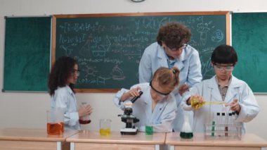 Kafkasyalı zeki öğretmen, meraklı öğrencilerin laboratuardaki deney kabına renkli sıvı dökmesini destekler. Yaratıcı çocuklar deney yapmaya ve biyokimyasal örnekleri incelemeye konsantre olurlar. Pedagoji.