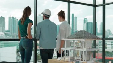 Gökdelene bakıp bir proje planı okurken, günlük kıyafetli akıllı mimar mühendis ekibi konuşuyor. Profesyonel yönetici takımı ev inşaatı hakkında beyin fırtınası yapıyor. Arkadan bak. İzleme