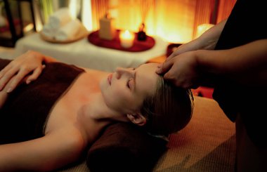 Beyaz kadın stres önleyici kafa masajı yapmaktan ve lüks otel veya otelde sıcak mum ışığında yüz güzelliği eğlencesi yapmaktan zevk alıyor. Sessiz.