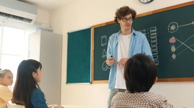 Matematik formülü veya teorisi ile karatahtanın önünde dururken sınıfın etrafına bakan profesyonel akıl hocası. Çeşitli ilköğretim öğrencileri matematik dersinde öğreniyor, çalışıyor ve oturuyor. Pedagoji.