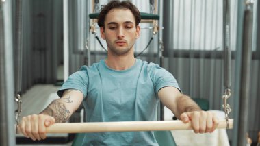 Man performing seated core exercise on pilates trapeze holding bar to strengthen arms and core muscles at gym. Trainer doing chest press on the cadillac for strengthening chest, shoulder. Habituate. clipart