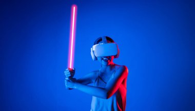 VR kulaklık takan zeki bir kadın metaevrene bağlanıyor, gelecekteki siber uzay topluluğu teknolojisi. Kılıç dövüşü oynarken lazer kılıcını sıkıca tutan zarif bir kadın. Halüsinasyon.