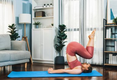Spor kıyafetleri içinde esnek ve becerikli bir kadın evde egzersiz paspası üzerinde meditasyon pozisyonunda yoga yapıyor. Huzurlu ve huzurlu bir yoga yaşam tarzı..