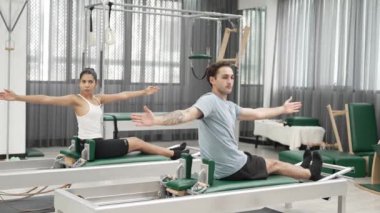 Pilates reformatör makinelerinde senkronize kol uzantıları yapan iki müşteri. Mutlu pilates partnerleri, esnekliği arttırmak ve dengeyi ve kontrolü sağlamak için reformcunun üzerine oturdular. Alışkanlık.