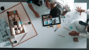 Mimar mühendis ekibinin tartıştığı ve tablet görüntüleme inşaatını planlı ve ev modeliyle toplantı masasında işaret ettiği en tepeden aşağı bakış açısı. Çeşitli tasarımcı tasarım evleri. Hizalama.