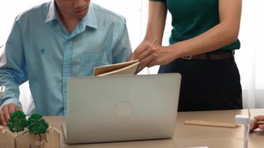 Yel değirmeni modeline ve ev şeklindeki bloğa danışmanlık yapan işadamları, Dünya Yöneticisi 'nin dizüstü bilgisayar üzerinde çalışmasını kurtarmak için yeşil enerji kullanımına referans olarak başvuruyorlar. Tanımlama.