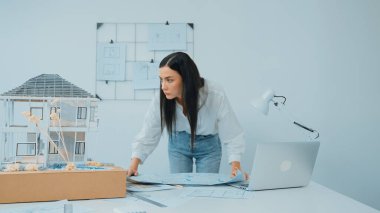 Genç, güzel beyaz bir mimar masanın üzerine plan koyar ve ev modeliyle karşılaştırırken, modern ofisteki fahişe modellerini dikkatlice incelerken arkadaki çizgilerle karşılaştırır. Tertemiz..