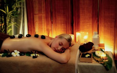 Lüks tatil köyündeki kaplıcalarda sıcak taş masajı, sıcak mum ışığı, spa bazalt taşı masajının keyfini çıkaran mutlu kadın müşteriler, rahatlatıcı bir sıcaklıkla vücudun üzerinde süzülüyorlar. Sessiz.