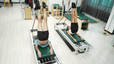 Müşteri, spor salonundaki yenilikçi bir makinede kayışla ters bacak kaldırma hareketi yapıyor. Çekirdek bağlantısını, dengesini ve esnekliğini geliştirmek için ters takla atan iki mutlu antrenör. Alışkanlık.