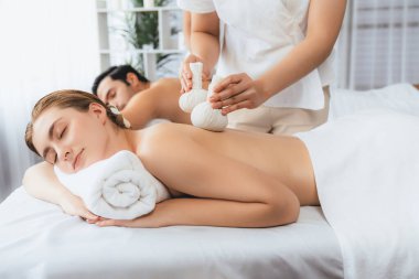 Sıcak bitkisel top spa masaj vücut tedavisi, masör nazikçe bitki torbasını çift müşteri vücuduna bastırıyor. Aromaterapi dinlenme sükuneti ve sükuneti kaplıca salonundaki atmosferi aydınlatıyor. Sessiz.