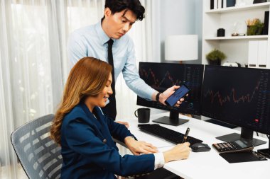 Gülümseyen işadamı cep telefonundaki dinamik borsa verilerini, iç ofisindeki internet sitesi uygulamasını analiz etmek için not yazan kadınlara gösteriyor. İnfobahn.