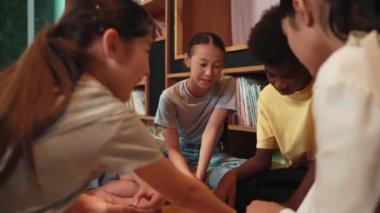 Tatlı kız en sevdiği kitabı sunmak için sayfayı çevirirken çocuğun daire içinde oturduğu arka plan. Çeşitli öğrencilerden oluşan bir grup modern kütüphanede fikir paylaşıyor. Yaratıcı aktivite. Öğretim