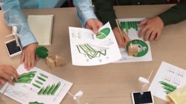 Eko evi projesini yel değirmeni tasarım modeli ve karbon ayak izini azaltmak için yeşil enerji kullanım grafiği ile toplantı masasında tartışan harika bir iş ekibi. Dünyayı kurtarın. Eline odaklan. Tanımlama.