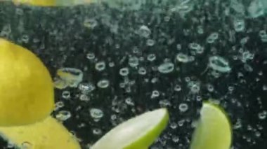 Bir bardak temiz suya düşen taze limon ve limon dilimlerini kapatın. Sarı limonlu makro dökülüyor ve koyu arkaplanlı suya dökülüyor. Makrografi. C vitamini Pabulum..