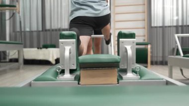 Esneklik ve dayanıklılığı artırmak için pilates reformcusu üzerinde diz çökme alıştırması yapan bir adam. Antrenör asistanı dengeyi arttırmak için yenilikçiye hamle yapıyor. Alışkanlık.