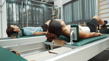 Vücut geliştirmek ve spor salonunda esnekliği arttırmak için çift pilates reformatörü üzerinde bacak egzersizi yapıyor. Pilates partneri bel kaslarını geliştirmek için pelvik köprü pozu veriyor. Alışkanlık.
